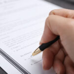 Woman signing last will and testament at grey table, closeup