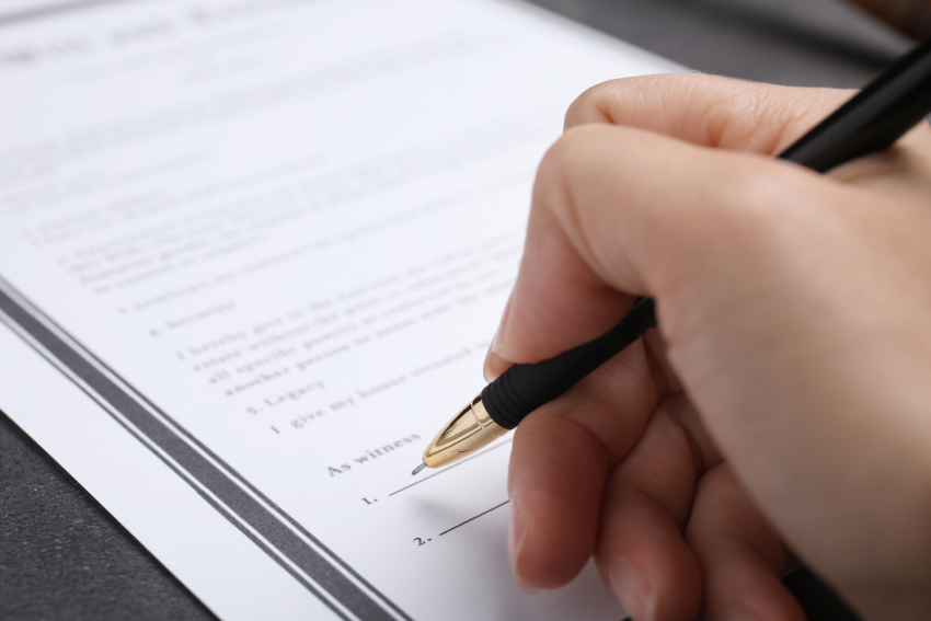 Woman signing last will and testament at grey table, closeup
